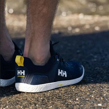 Close-up of a person's feet wearing black Helly Hansen athletic shoes on a gravel surface outdoors.